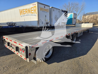 Drop deck trailer with Werner moving logo trailer and reflective edge markings; visible text includes 'WERNER' on the side of a box trailer in the background and 'DROP-DECK' style equipment; no other legible data visible.
