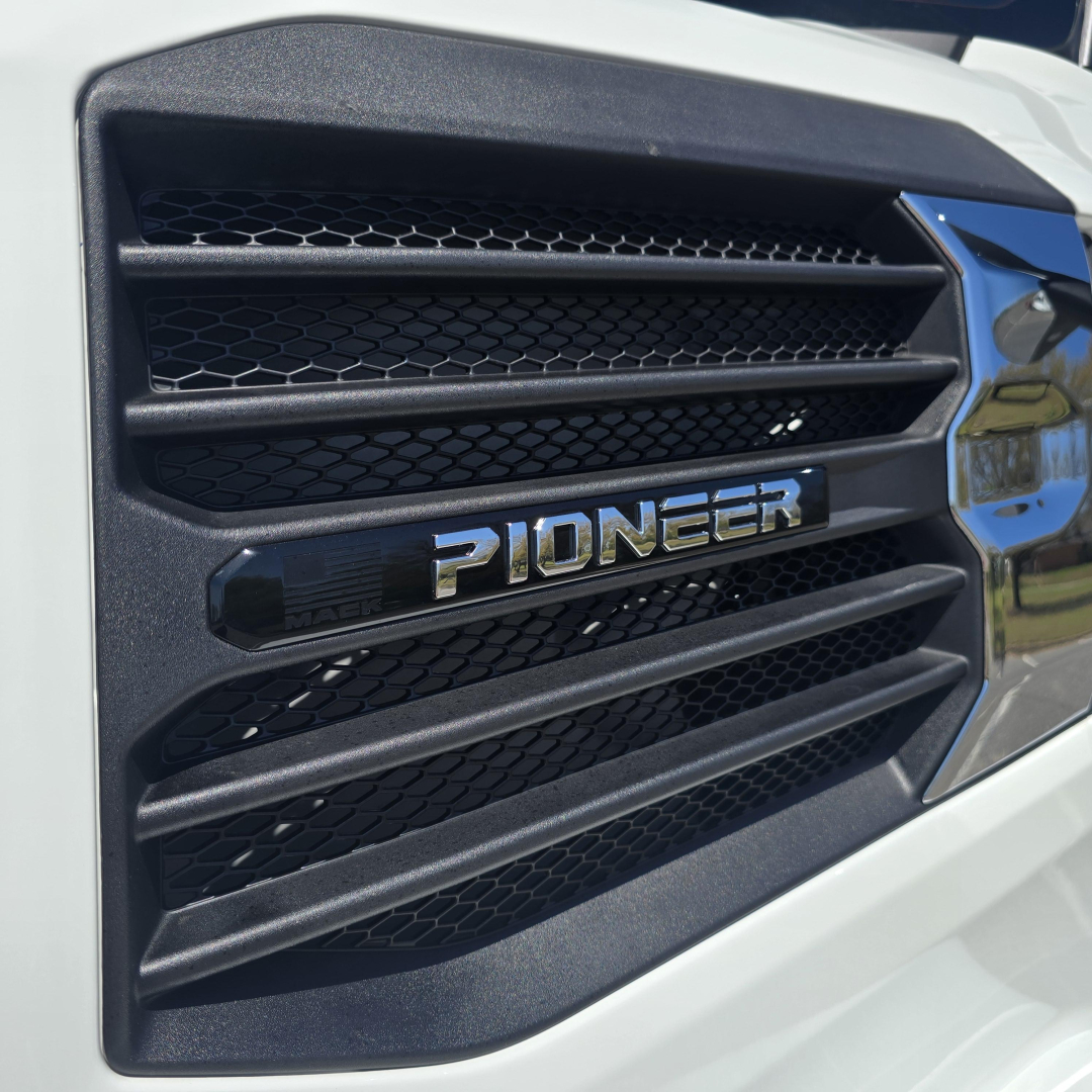 Front grille of a white Mack truck showing 'PIONEER' emblem and horizontal slats.