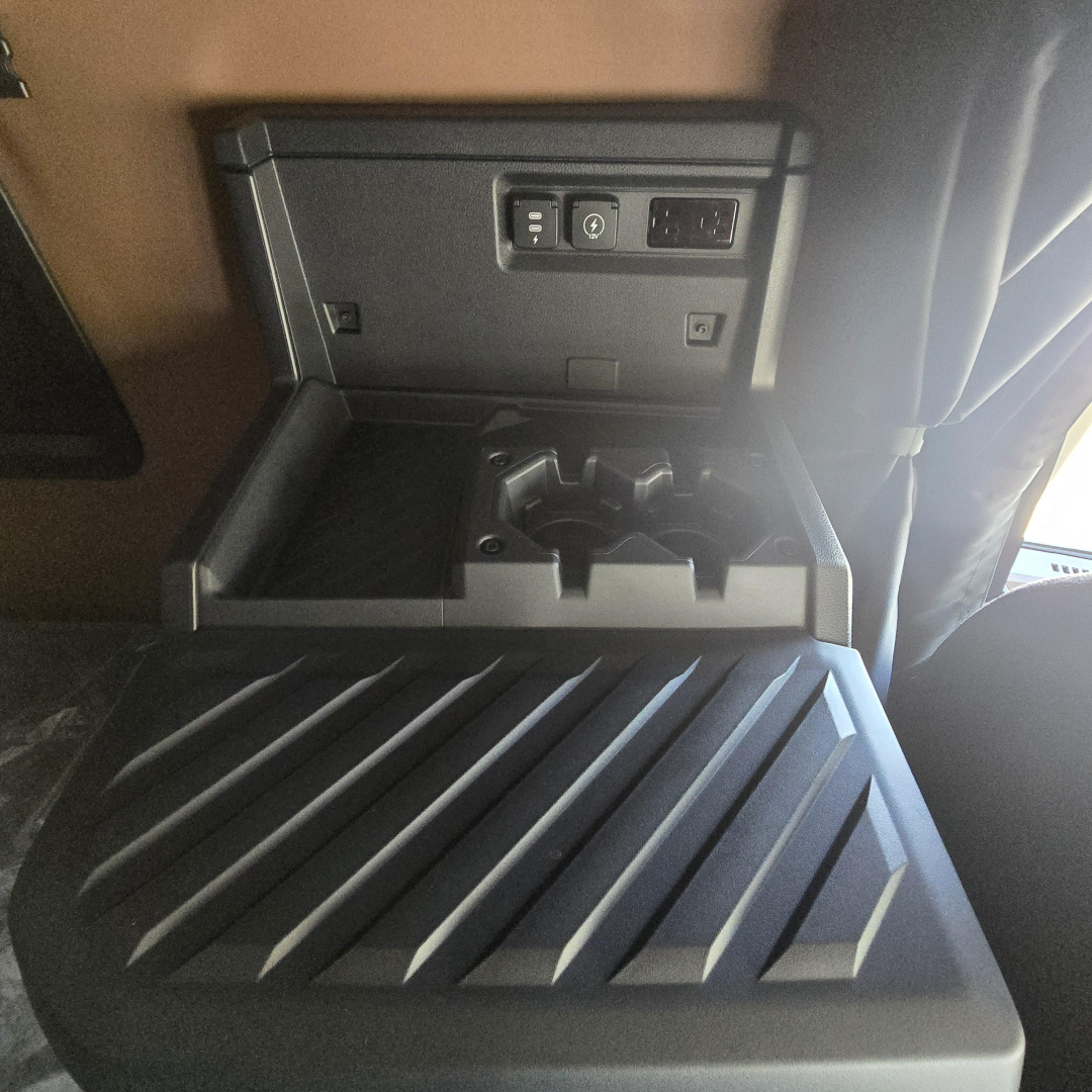 Truck cab interior showing storage console with USB/12V outlets and cup holders in the dash area of a 2027 Mack PR64T76M.