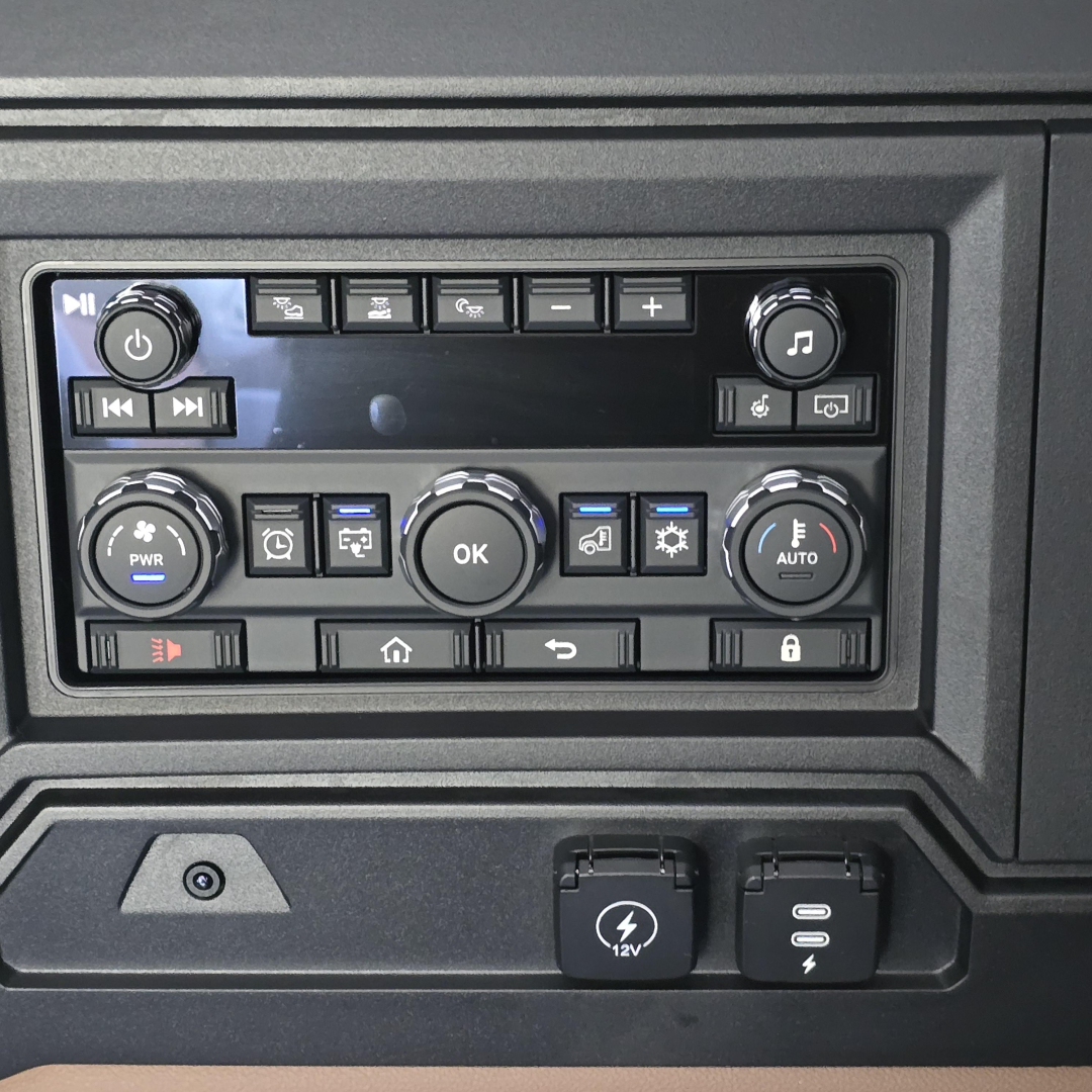 Dashboard control panel of a 2027 Mack PR64T76M showing steering wheel area, knobs, buttons, and 12V power outlet.