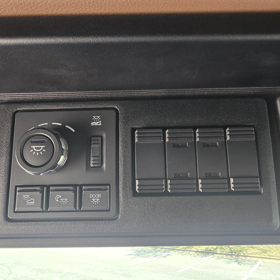 Dashboard controls with circular headlight dimmer and four rectangular switches on a Mack PR64T76M truck interior.