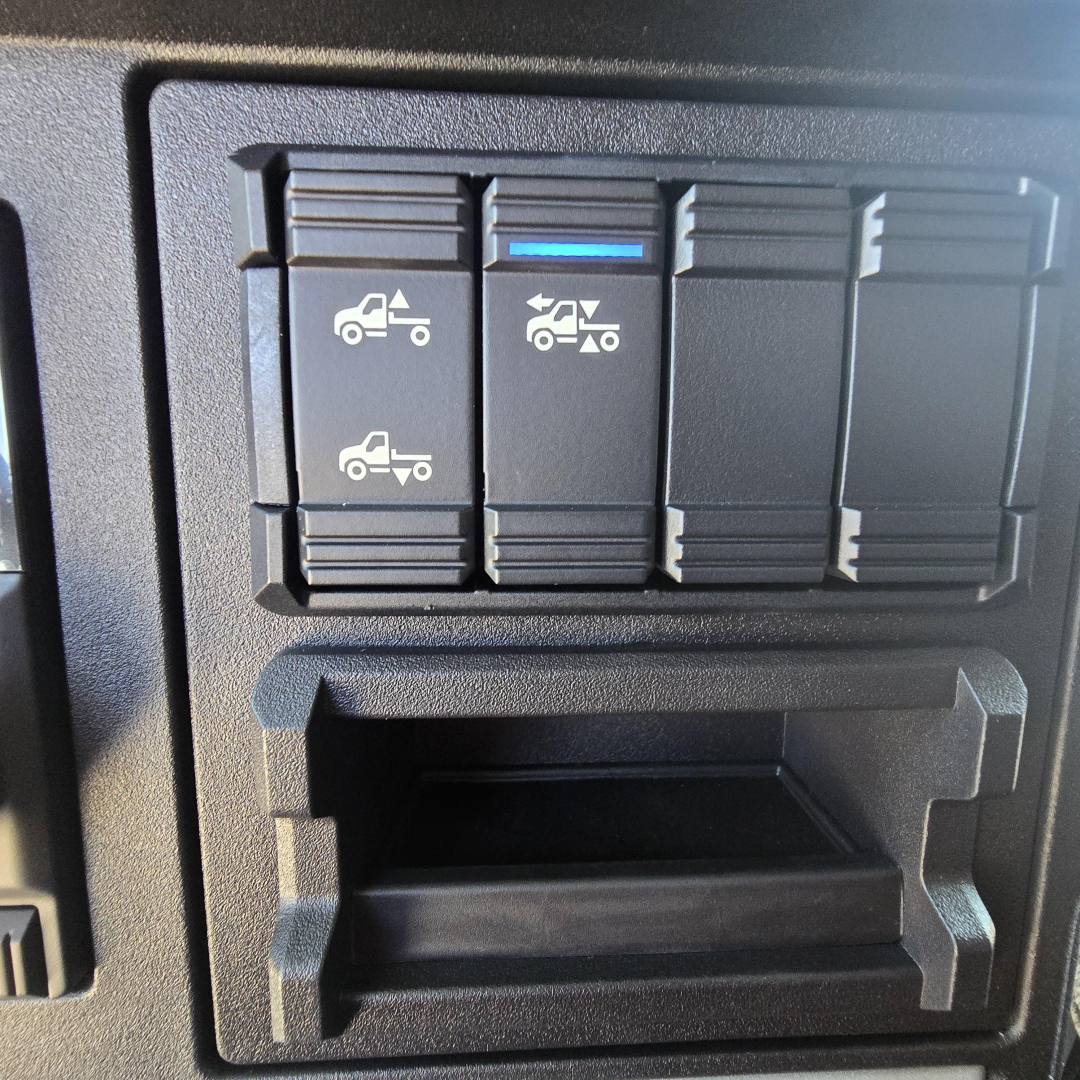 Dashboard switch panel with multiple rocker switches and a blue indicator, plus a small open storage pocket in a Mack truck cab interior.
