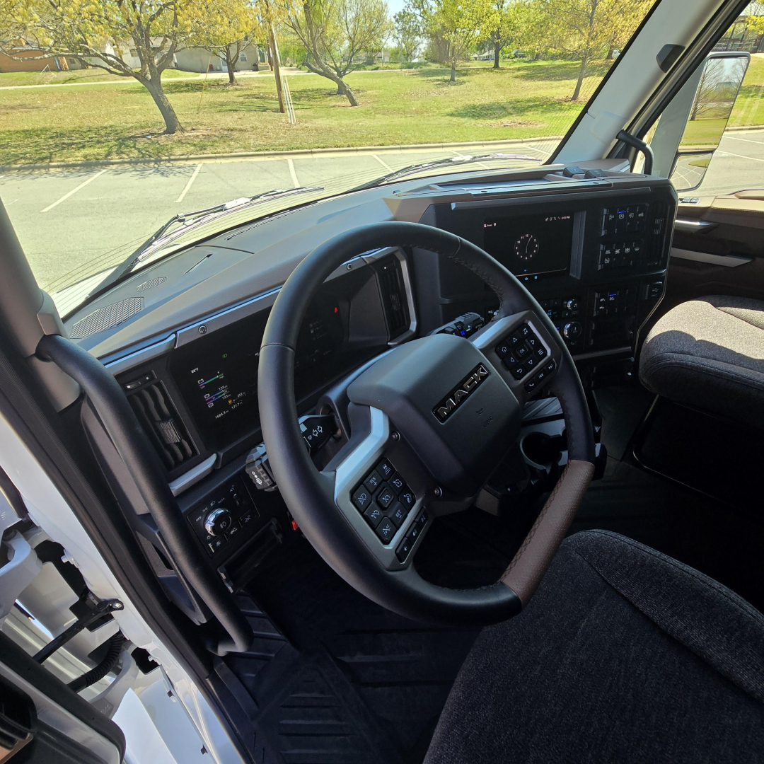 Cab interior of a 2027 Mack PR64T76M truck showing steering wheel with controls and dashboard display in a right-hand drive setup.