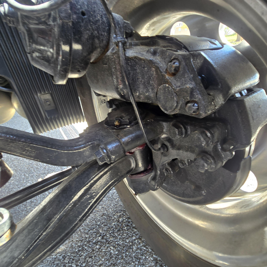 Rear axle and suspension components of a Mack truck, drive shaft, leaf spring, and wheel hub visible with hydraulic lines and metallic fittings.
