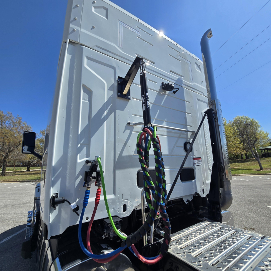 Back of a white Mack PR64T76M sleeper truck showing multicolor air lines and hoses connected to rear cab area.
