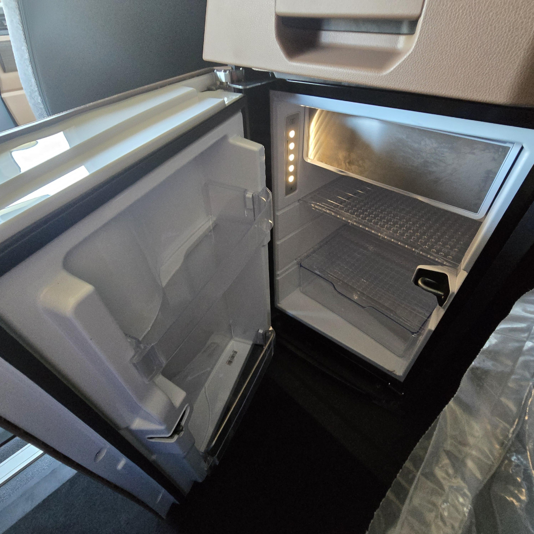 Refrigerator/freezer in a Mack PR64T76M truck cab with open door showing interior shelves and lighting.