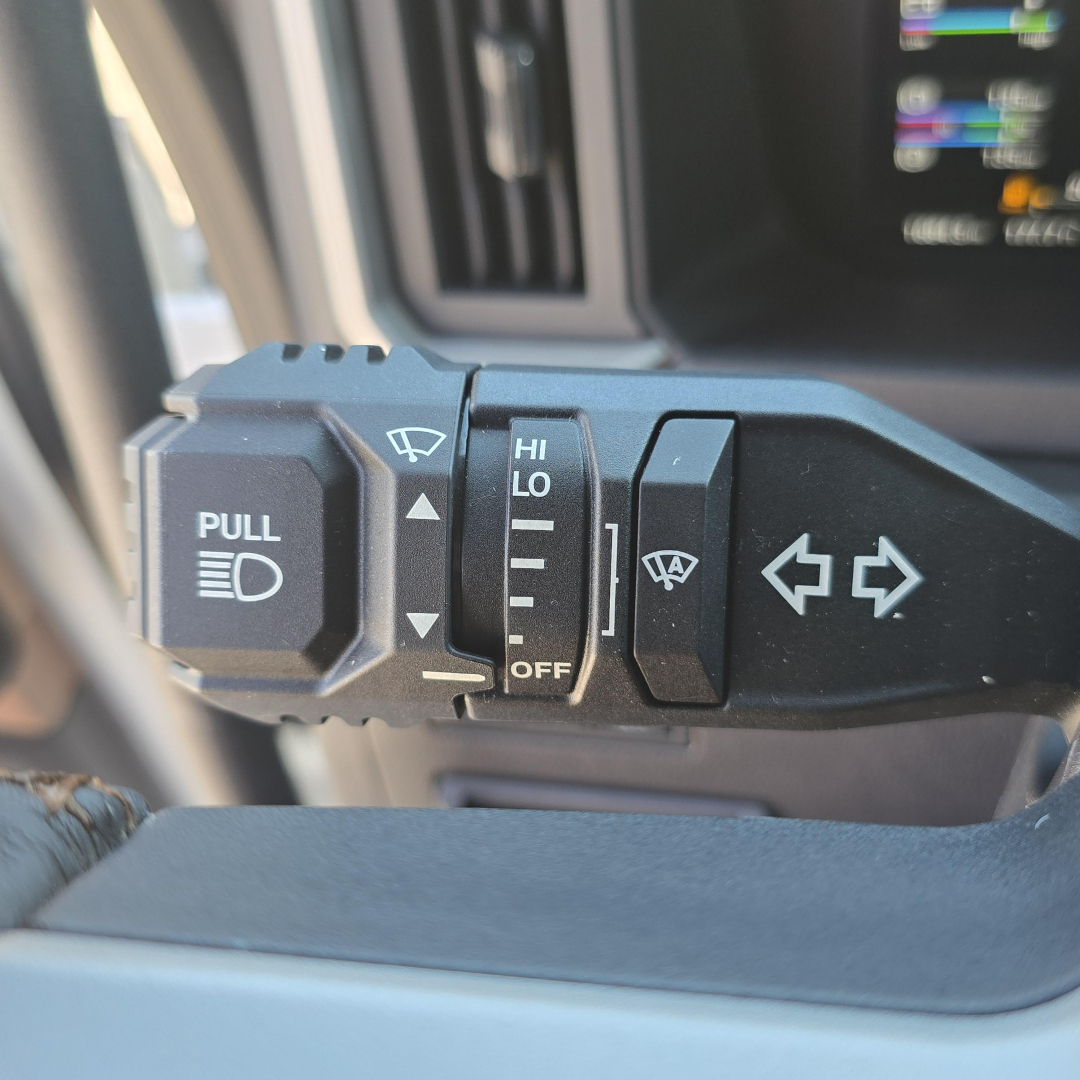 Steering column stalks with windshield wiper and light controls visible in a Mack truck interior, including a pull stalk and hi/lo switch.