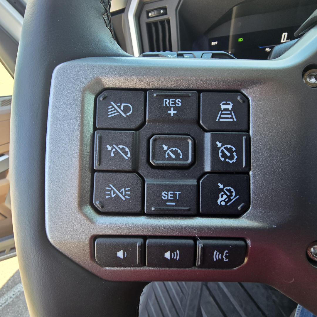 Truck steering wheel controls with multiple buttons including cruise, lane-keep assist, and volume on a Mack PR64T76M interior image.