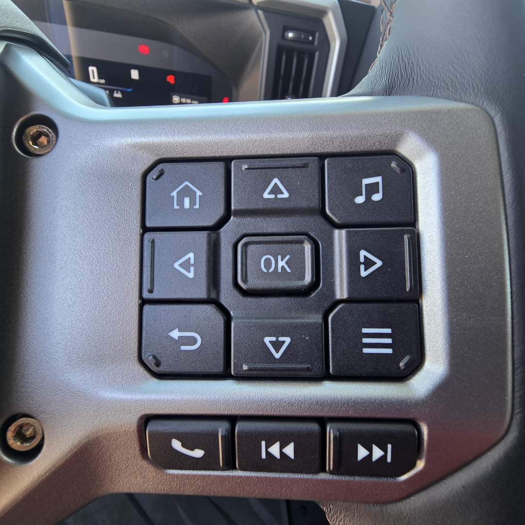 Mack PR64T76M truck steering wheel controls with navigation pad and media buttons visible in cabin.