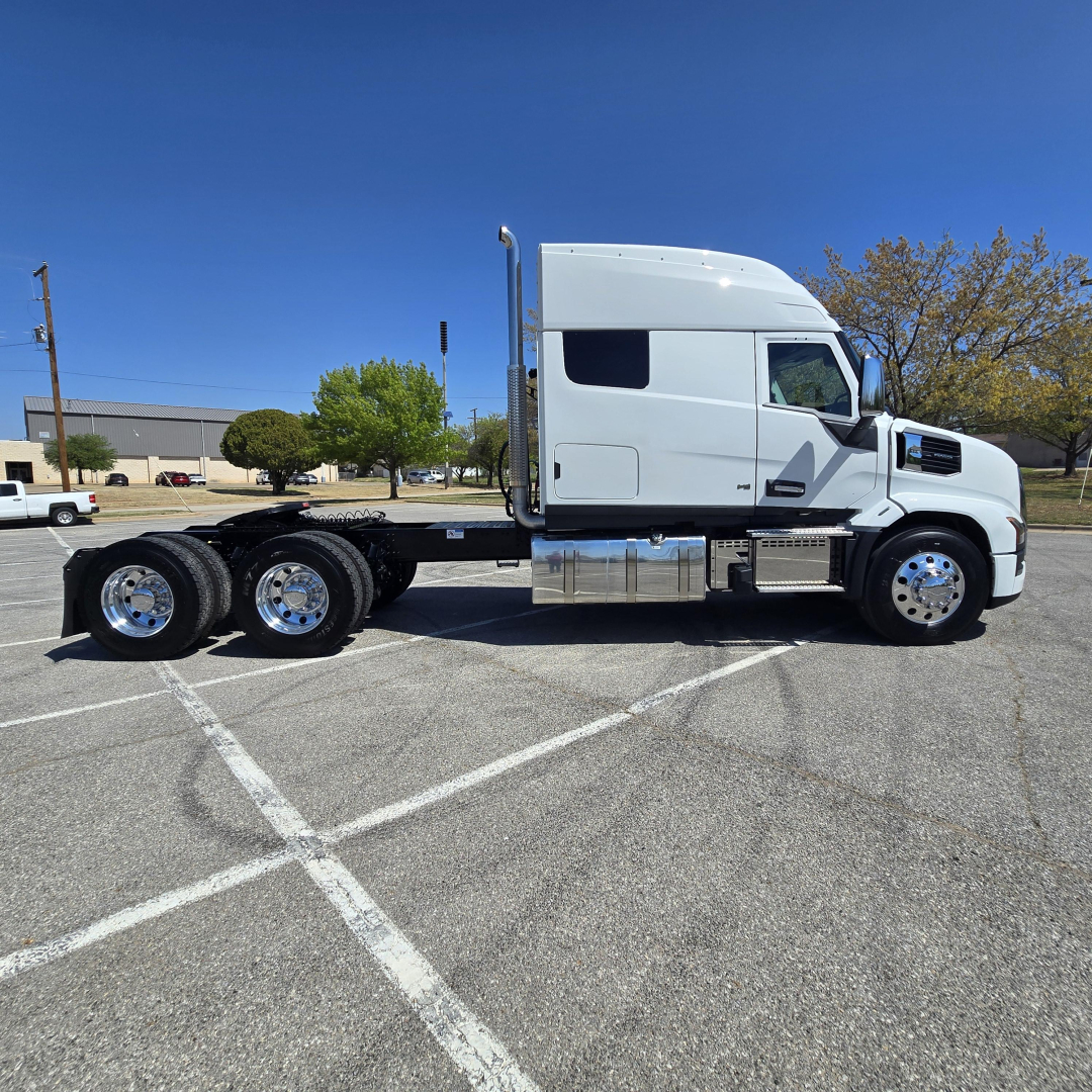 Truck chassis with tandem rear axles in-side view showing cab and fuel tanks.