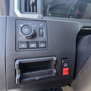 Mack PR64T76M dashboard area showing headlight control dial and auxiliary switches with a red SAVE button; blank storage pocket visible.