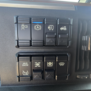 Dashboard control switches panel in a Mack truck showing various symbols including traction control, parking brake, and front axle/drive mode indicators.
