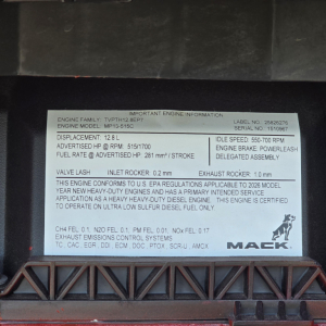 Engine information plate on Mack MP engine bay showing model MP13-515C with 12.8 L displacement, HP/RPM 515/1700, idle 550-700 RPM, inlet rocker 0.2 mm, exhaust rocker 1.0 mm, fuel rate at advertised HP 281 m3? / stroke, engine family TVPTH