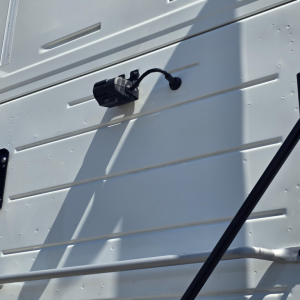 Truck exterior showing a black electrical connector with cable on a white panel siding.