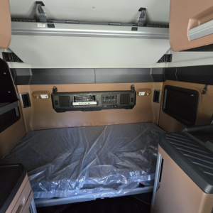 Mack PR64T76M truck sleeper cab interior showing control panel and storage compartments. Dashboard with radio, vents, and window shades; brown upholstery