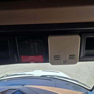 Truck interior dash area showing a beige sun visor/cover with vent slots and a warning label, windshield view ahead, front hood visible.