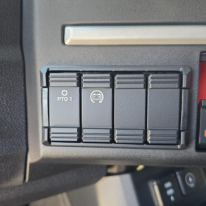 Panel of switches in Mack PR64T76M truck showing PTO1 button and a circular icon switch and blank slots