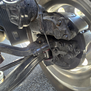 Rear axle and suspension components of a Mack truck, drive shaft, leaf spring, and wheel hub visible with hydraulic lines and metallic fittings.