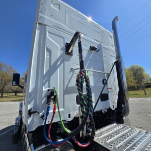 Back of a white Mack PR64T76M sleeper truck showing multicolor air lines and hoses connected to rear cab area.