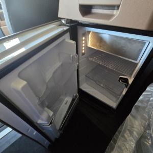 Refrigerator/freezer in a Mack PR64T76M truck cab with open door showing interior shelves and lighting.