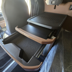 Truck interior showing storage drawer in a Mack PR64T76M sleeper cab, with open tray/compatibility shelf and dash-side console; visibility of cabin seating and control shelf.