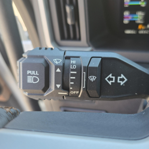 Steering column stalks with windshield wiper and light controls visible in a Mack truck interior, including a pull stalk and hi/lo switch.