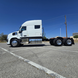 Truck chassis and cab of a white 2027 Mack PR64T76M sleeper with dual rear axles, side fuel tanks, and chrome wheels.