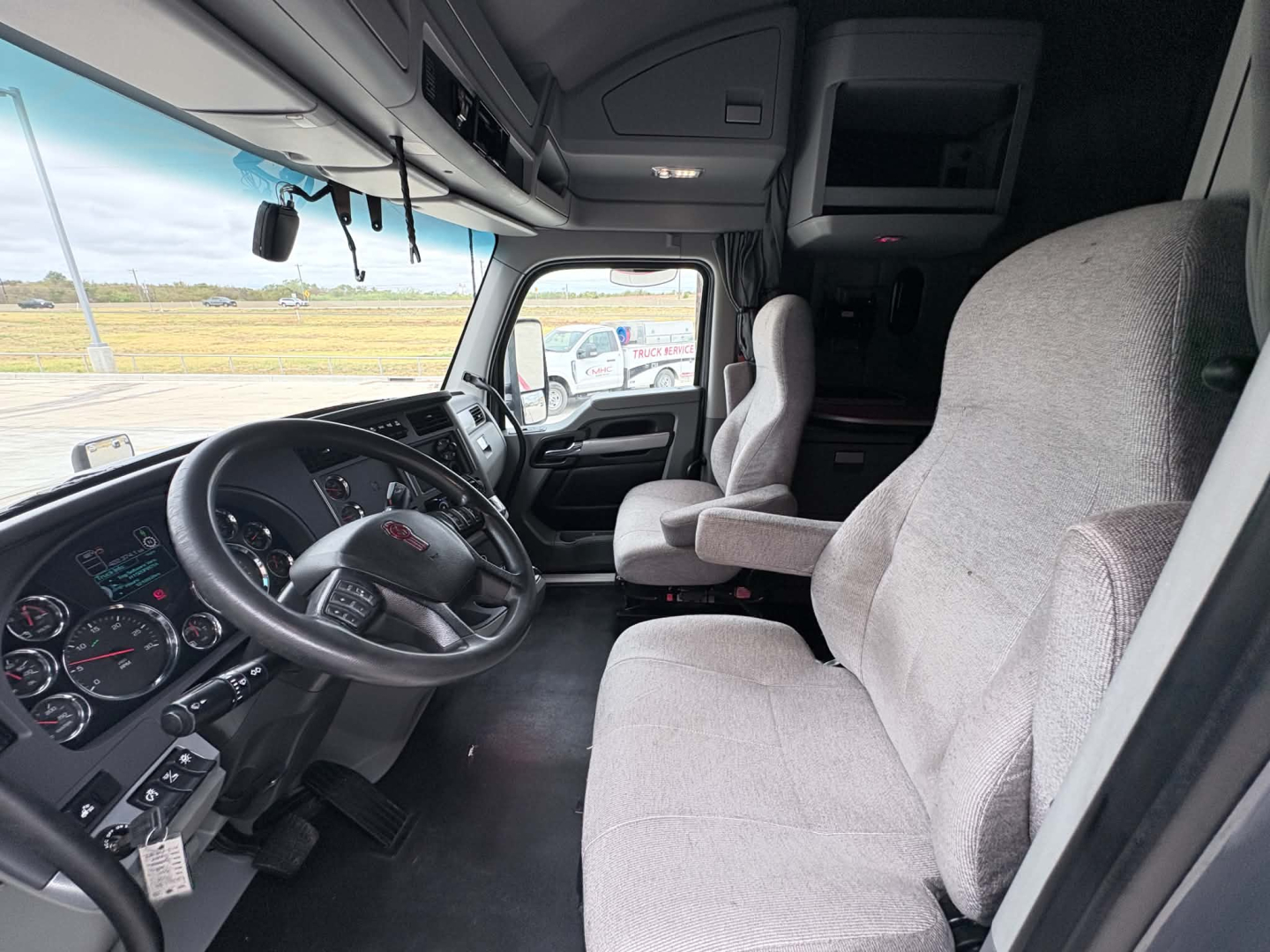 Kenworth T680 truck cab interior showing steering wheel, dashboard gauges, two front seats, and overhead storage.