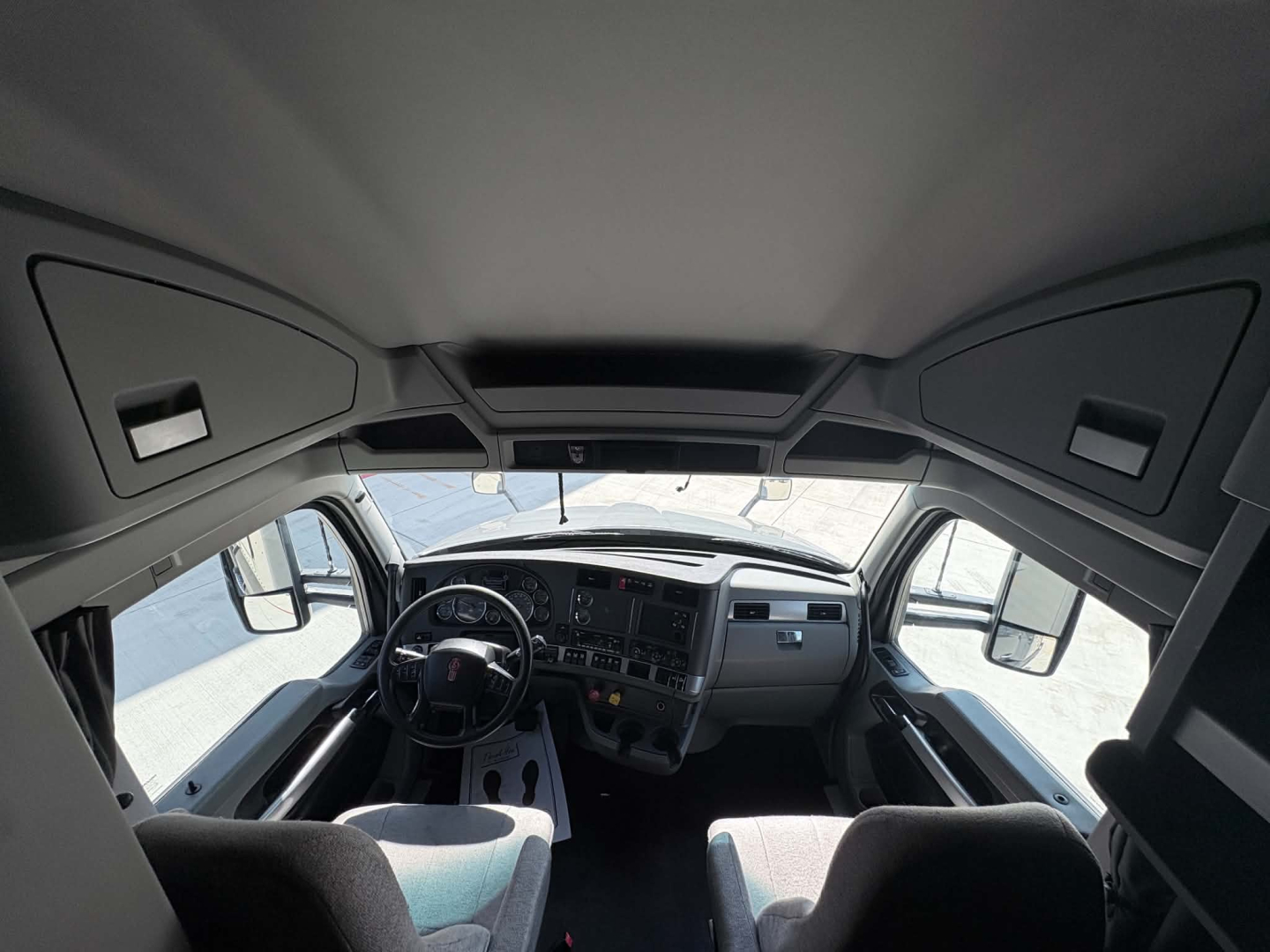 Kenworth T680 cabin interior view from windshield showing steering wheel and dashboard in-right and driver seat.