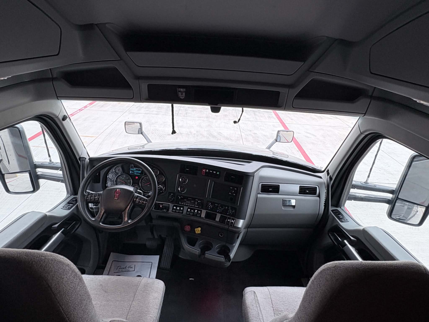 Kenworth T680 truck cabin dashboard and steering wheel interior in-view showing steering wheel, instrument panel, and seats.