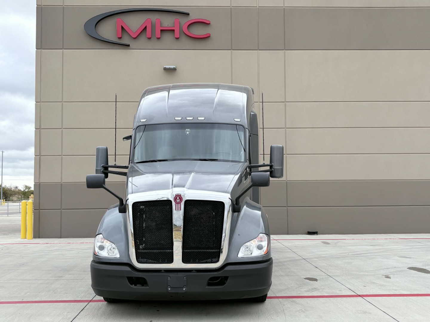 Kenworth T680 conventional sleeper truck front view in service lot, dual black grille, large windshield, side mirrors, gray exterior.