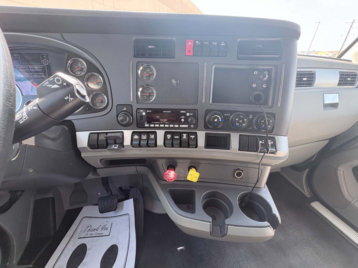 Interior dash of a Kenworth T680 truck showing gauges, steering wheel, control switches, and center console with ignition key and knobs.