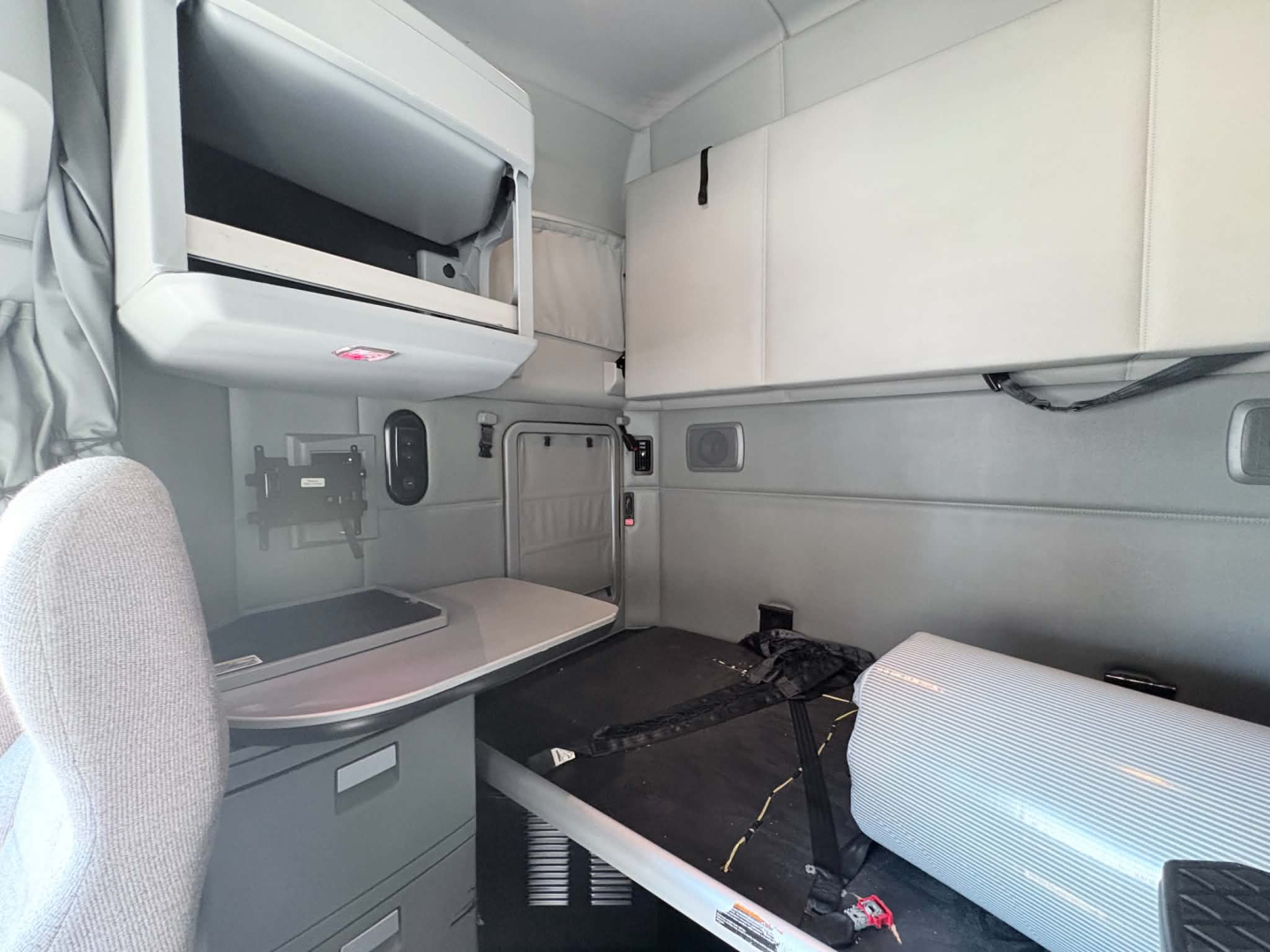Kenworth T680 sleeper cab interior showing bunk area and overhead storage with dashboard controls not visible.