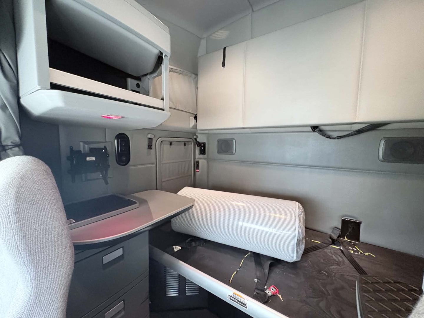 Kenworth T680 sleeper cab interior showing countertop, storage cabinets, and bed area with white foam pillow/bolster.