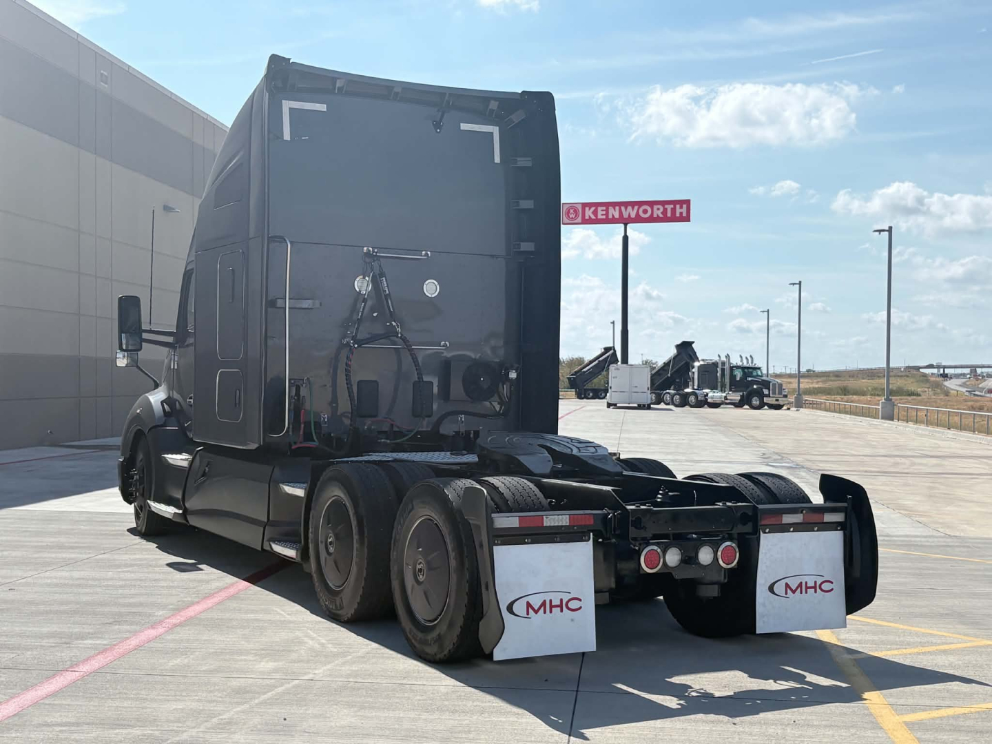Kenworth T680 tractor rear view showing fifth wheel, rear fenders, and mud flaps with MHC logo.