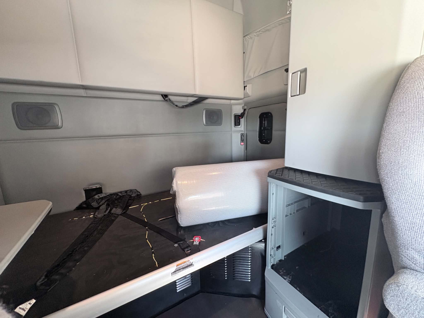 Kenworth T680 cab interior showing sleeper bunk and storage area with mattress, side cabinet, and seating.