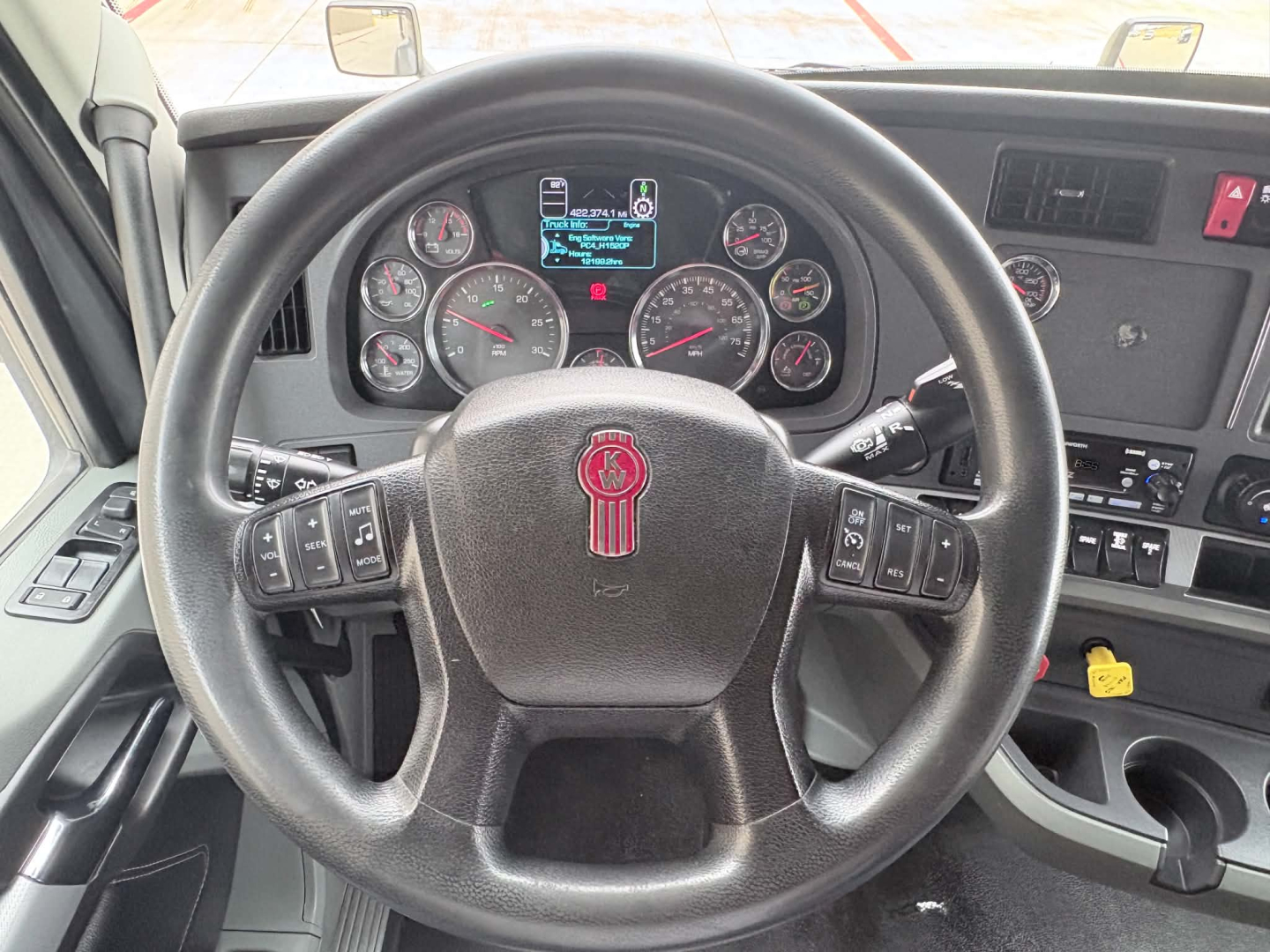 Kenworth T680 steering wheel and instrument cluster with gauges visible through the steering wheel, dashboard controls on the right, and a small digital display in the center.