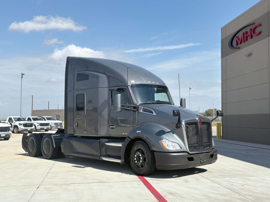 Kenworth T680 sleeper cab tractor in dark gray, side view showing aerodynamic mirrors and front grille. Visible stock number 0632139, warehouse background.