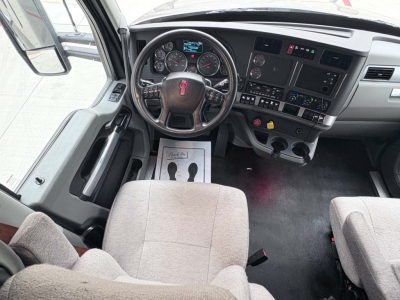 Kenworth T680 cab interior showing steering wheel with red emblem, instrument cluster, dashboard controls, and two front seats.