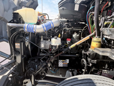 Truck engine bay of a 2022 Kenworth T680 with visible hoses, wiring, coolant reservoir, and various engine components.