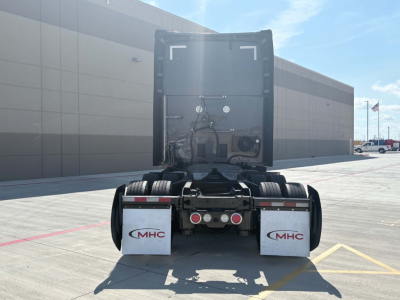 Kenworth T680 tractor rear view showing fifth wheel hitch and dual rear mud flaps with MHC logo in a parking lot.