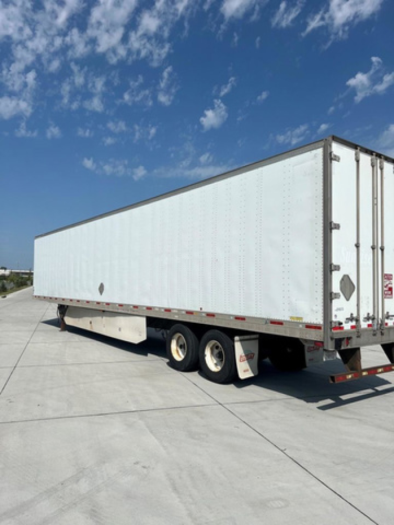 semi-trailer with white box and tandem axles parked on a concrete surface under blue sky.