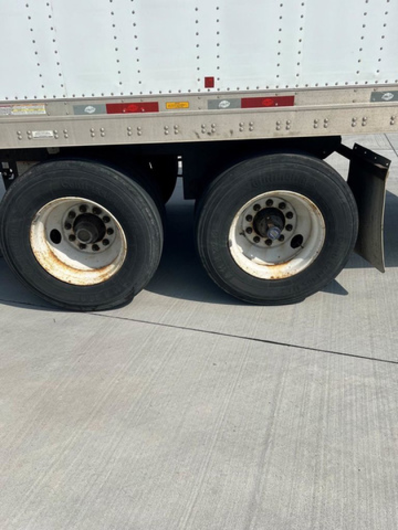 Trailer wheels and side of a utility van trailer showing dual rear axles and tire rims.