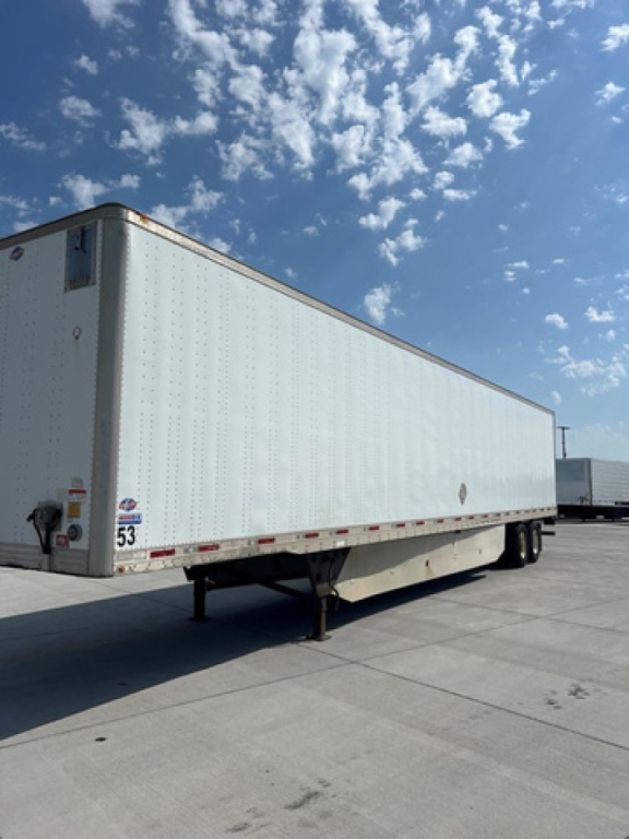Utility van trailer side view showing long white box with riveted panels and wheel area in background; undercarriage and landing gear visible.