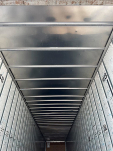 Interior of trailer van showing metal ceiling ribs and side walls with corrugated texture.