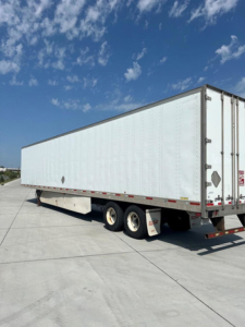 semi-trailer with white box and tandem axles parked on a concrete surface under blue sky.
