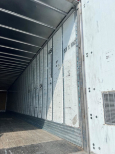 Trailer van interior side wall with ribbed metal panels inside a cargo trailer.