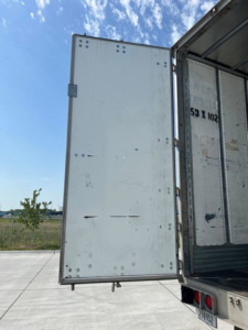 Rear door of a utility van trailer open, showing interior wall with vertical seams and rivets.