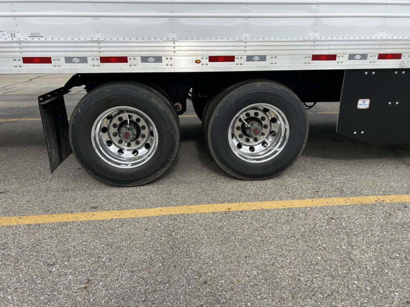 Dual rear wheels of a refrigerated trailer with chrome rims, black mudguard, and side panels visible