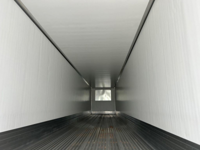 Interior of a refrigerated trailer with white steel walls, black floor, and a small rear door/platform apparent at far end.